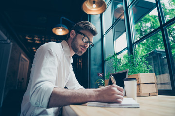 Yow angle view of a young stylish well dressed author writer is working in a modern coworking, writing the novel, in glasses, so serious and focused