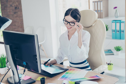 Intelligent young asian graphic designer is working with computer and colors samples, stylus, smiling. She is a successful self employed artist