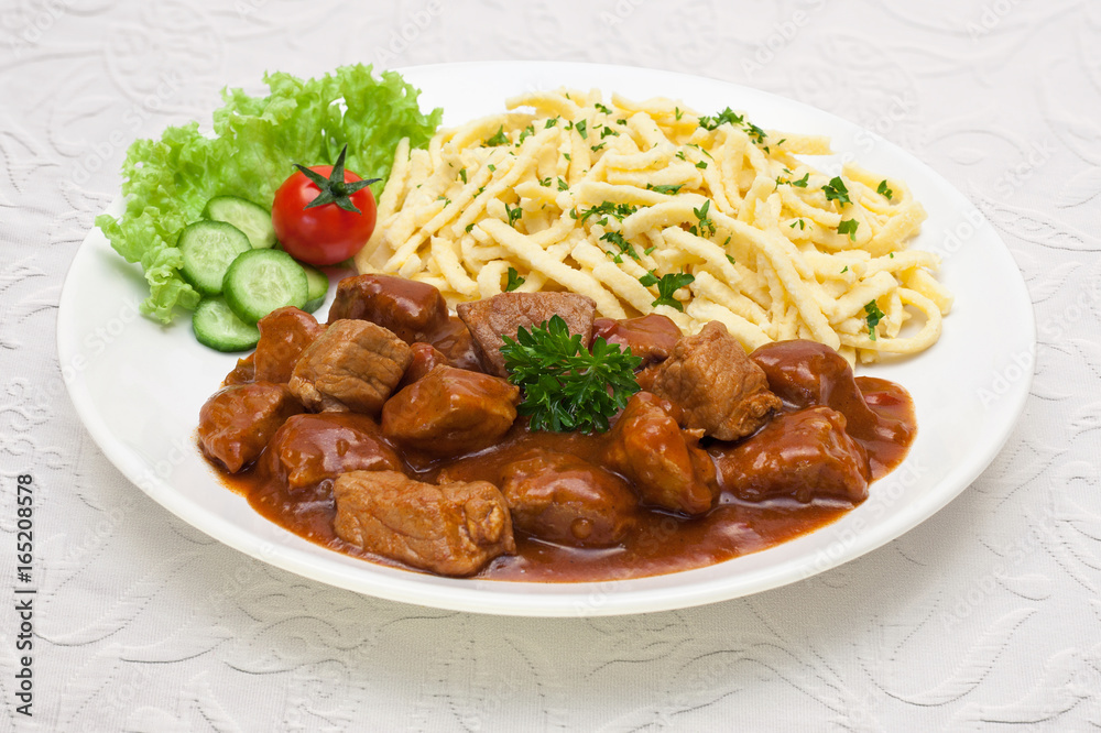 Stock-Foto „Gulasch mit Spätzle - Tellergericht auf weißer Tischdecke“