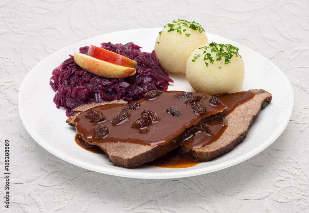 Stock-Foto „Sauerbraten mit Rotkohl und Knödeln - Tellergericht auf weißer Tischdecke“