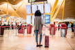 © DavidPrado - Black Woman looking at the timetable information panel in the airport with a suitcase