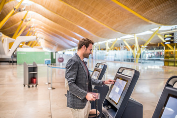 happy man using the check-in machine at the airport getting the boarding pass.