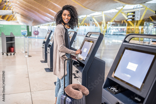 happy black woman using the check-in machine at the airport getting the boarding pass.