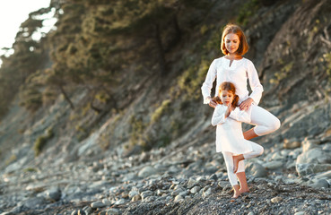 Wall Mural - Happy family mother and child doing yoga, meditate in lotus position on beach