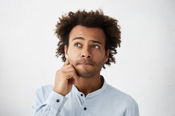 Wall Mural - Close up portrait of forgetful and clueless dark-skinned student with stubble touching face, trying to recollect line while declaiming poem in front of class, looking away, primming up his lips