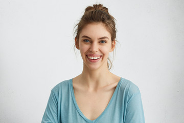 Wall Mural - Happy smiling female with attractive appearance and dark hair tied in knot wearing blue blouse showing her broad smile having good mood liking to pose at camera. Happiness, positiveness concept