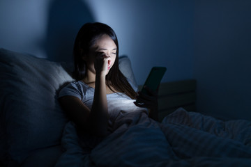 Wall Mural - Woman feeling eye pain with using mobile phone on bed