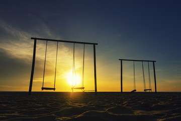 Wall Mural - set of swing on the sandy beach over sunrise background