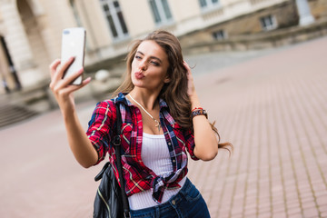 Wall Mural - Brunette woman taking selfie with mobile phone walking along the street with backpack