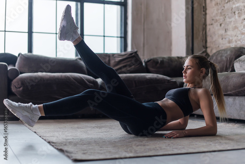 Fotografía Young sporty female doing abs workout in living room performing alternate leg ra