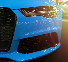 Front view of blue modern luxury sport with soft orange sun light. Car exterior details. Headlight of a modern sport car. The front lights of the car