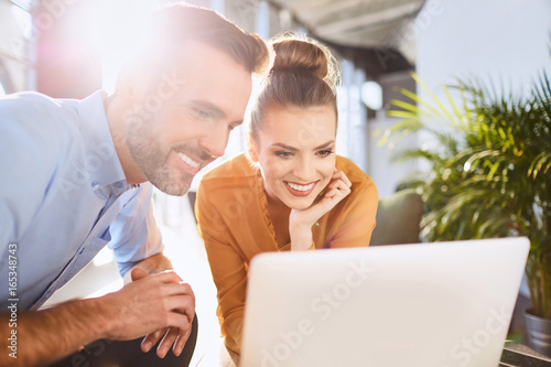 Cuadros en Lienzo Two cheerful coworkers sitting in company lobby and looking at laptop