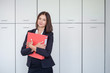 © Maxim - Happy young businesswoman holding a red binder And smiling