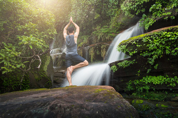 Young man meditating and relax in lotus position while doing yoga on the rock between waterfalls