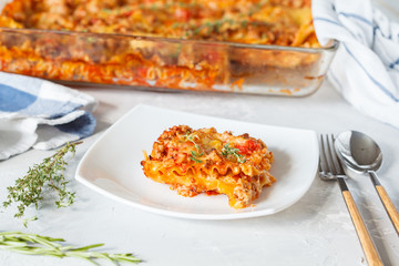 Wall Mural - Traditional Italian lasagna baked with herbs and a piece of lasagna on a white plate.