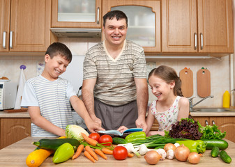 Father and two children reading cooking book and choice dishes. Happy family, girl and boy having fun with fruits and vegetables in home kitchen interior. Healthy food concept.