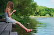 © boomeart - Side view of a girl sitting on wooden pier on river bank and messaging. Beautiful woman with hair blown with the wind.