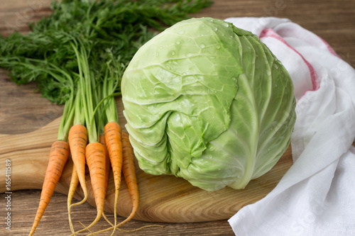 Fresh young cabbage and carrots with greens for coleslaw salad on a wooden board on a wooden table, selective focus Poster Mural XXL