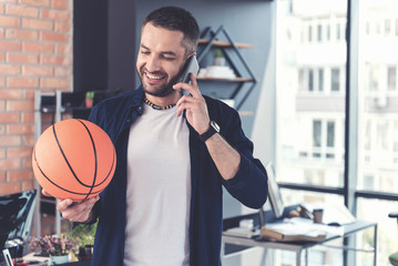 Wall Mural - Positive adult employee is talking on smartphone and expressing gladness