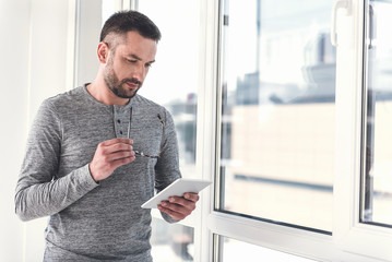 Wall Mural - Pleasant guy with stubble is analyzing information using gadget