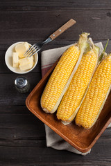 Wall Mural - Fresh corn on the cob with salt and butter on wooden table, closeup, top view. Dark background