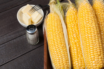 Wall Mural - Fresh corn on the cob with salt and butter on wooden table, closeup, top view. Dark background with copy space