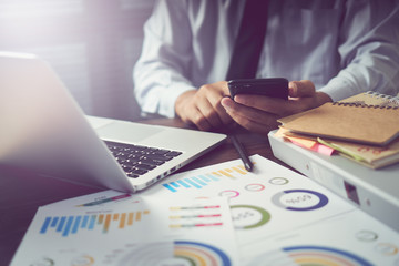 businessman hand working smart phone on wooden desk in office in morning light. The concept of modern work with advanced technology. vintage effect