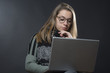 © alex.pin - Giovane ragazza bionda con occhiali e maglia a righe, con il suo computer tra le gambe guarda seria - sfondo nero