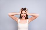 Fototapeta  - Stop it! No! Crazy yelling teen is messing her hair. She is in a casual white singlet on a pure light background, screaming and being very angry, uncontrollable