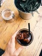 Glass of coldbrew on wooden table, woman hand holds a cup, home plants and sugar