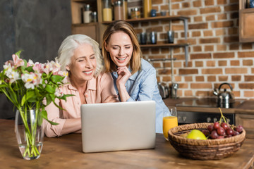 two women, senior and young using laptop at table in kitchen