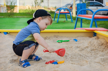 Charming cute boy playing in the sandbox on the playground