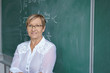© contrastwerkstatt - lächelnde, ältere lehrerin steht vor der tafel