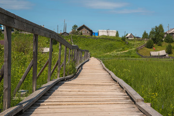  north Russian village Isady. Summer day, Emca river, old cottages on the shore, old wooden bridge and clouds reflections.