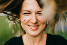 Closeup Portrait Of Young Happy Mother Smiling Girl With Narrowed Eyes Looking At Camera And Throwing Up Long Hair. Motion Blur. Emotional And Kind Expressive Face. Abstract Background. Summer Nature