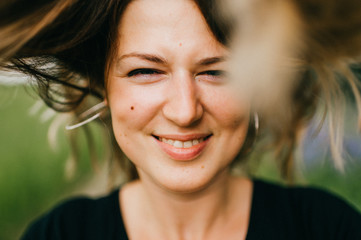 Closeup portrait of young happy mother smiling girl with narrowed eyes looking at camera and throwing up long hair. Motion blur. Emotional and kind expressive face. Abstract background. Summer nature