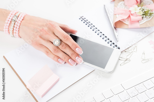 Plakat zbliżenie widok kobiece strony z pięknym manicure i biżuteria trzymając smartfon w miejscu pracy
