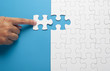 © Burhanuddin - Hand holding piece of white puzzle on blue background. Business and team work concept.