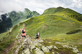 Fototapeta Góry - man and woman running together on beautiful high mountain trail with clouds after summer storm