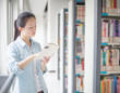 © onlyyouqj - Portrait of a smiling young student reading a book in a library