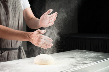 Wall Mural - woman baker sprinkled flour on roll dough on a wooden board. Process of preparing pizza. Cooking time, cooking concept, selective focus