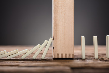 Wooden Block Amidst Falling And Upright Domino Pieces On Table