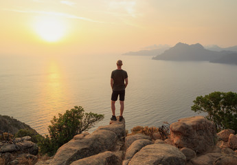 Man looking at the sunset over the Golf of Porto from the rocks near the famous Chateau Fort. Corsica, France.