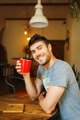 Wall Mural - Red cup in the hands of a smiling Handsome