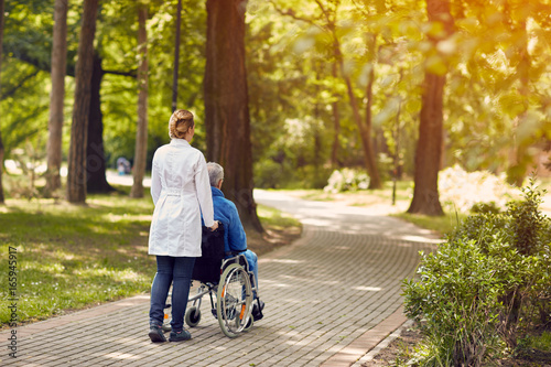 Fotografía nurse helping elderly man on wheelchair outdoor.