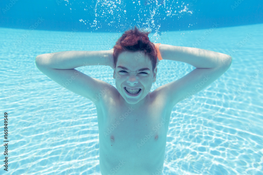 Teenage boy having fun, diving underwater at spa resort swimming pool ...