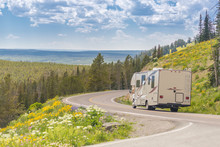 Camper Driving Down Road In The Beautiful Countryside Among Pine Trees And Flowers.