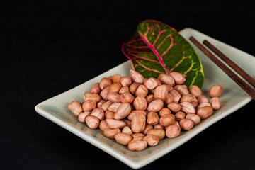 ground nut in green dish with chopstick on black background