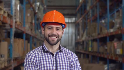 Poster - Portrait worker in warehouse at work. Happy friendly young man with beard looking at the camera with smile. smiling manager in storehouse wearing casual shirt and orange hard hat.