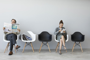 Man reading newspaper and woman using digital tablet